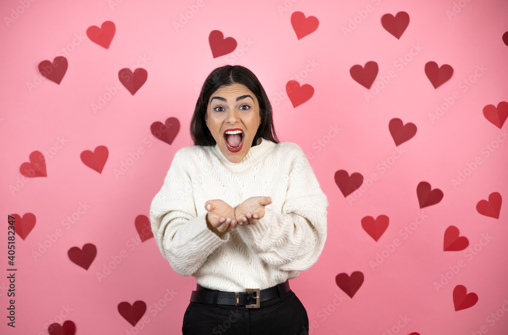 Young beautiful woman over pink background with harts Smiling with hands palms together receiving or giving gesture. Hold and protection Young beautiful woman over pink background with harts Smiling with hands palms together receiving or giving gesture. Hold and protection