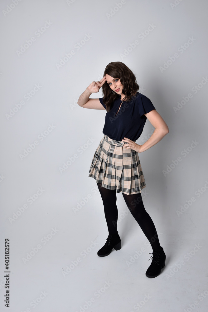 Full length portrait of pretty brunette woman wearing tartan skirt and blouse. Standing pose on the ground, against a studio background. Full length portrait of pretty brunette woman wearing tartan skirt and blouse. Standing pose on the ground, against a studio background.