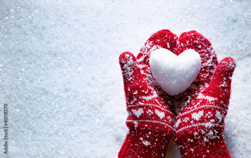 Female hands in knitted mittens with snowy heart against snow background photo
