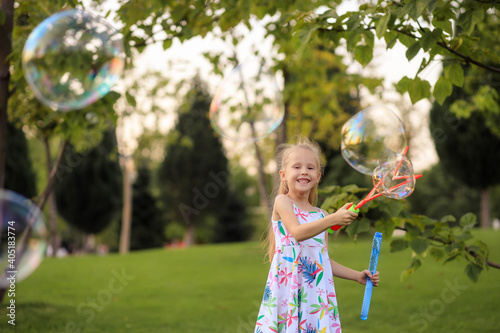 Happy little girl playing with summer soap bubbles in the park.