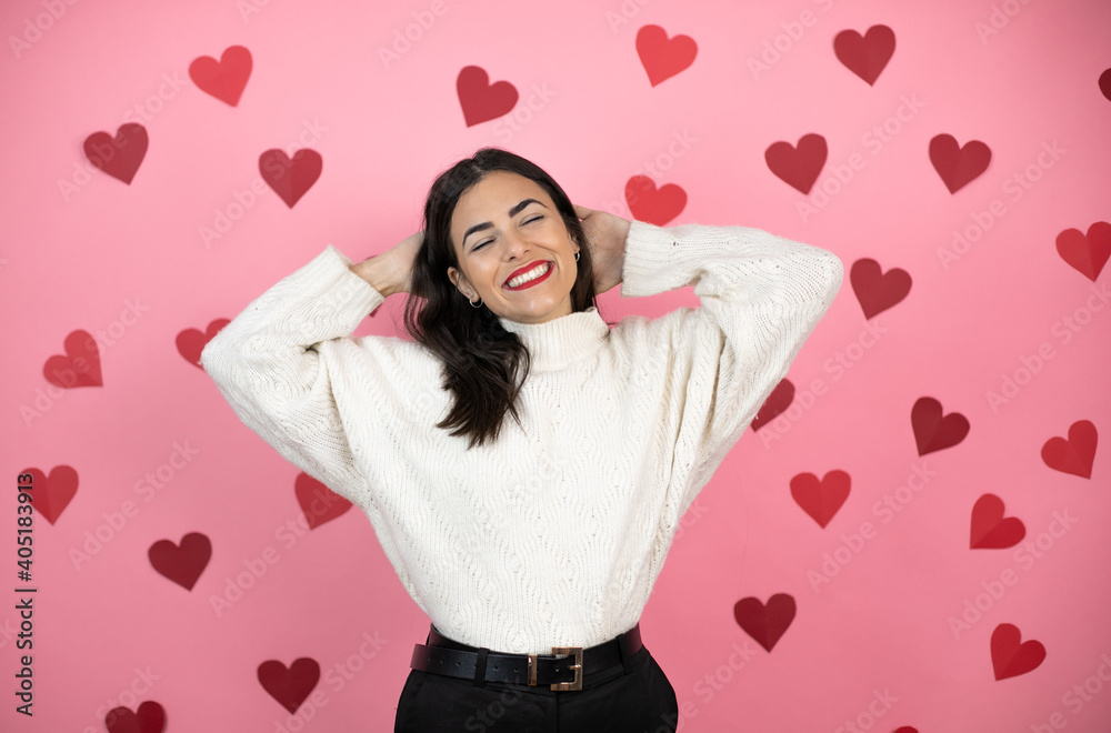 Young beautiful woman over pink background with harts relaxing and stretching, arms and hands behind head and neck smiling happy Young beautiful woman over pink background with harts relaxing and stretching, arms and hands behind head and neck smiling happy