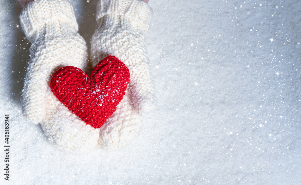 Fototapeta premium Female hands in knitted mittens with red heart against snow background