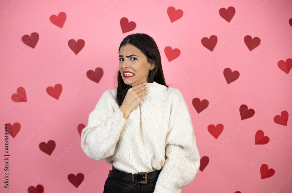 Young beautiful woman over pink background with harts touching painful neck, sore throat for flu, clod and infection Young beautiful woman over pink background with harts touching painful neck, sore throat for flu, clod and infection