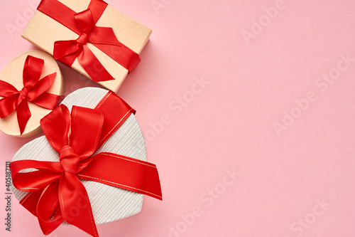 Gift box in the form of heart with a red ribbon on pink background. Valentines day concept postcard. Top view.