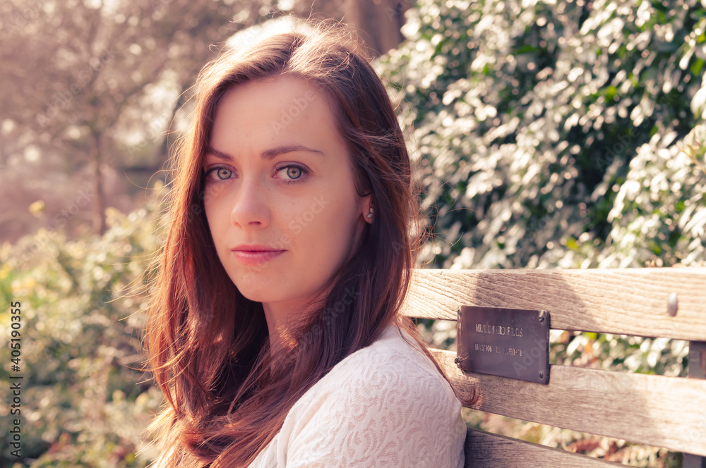 Naklejka premium Portrait of young woman sitting on park bench in soft sunlight