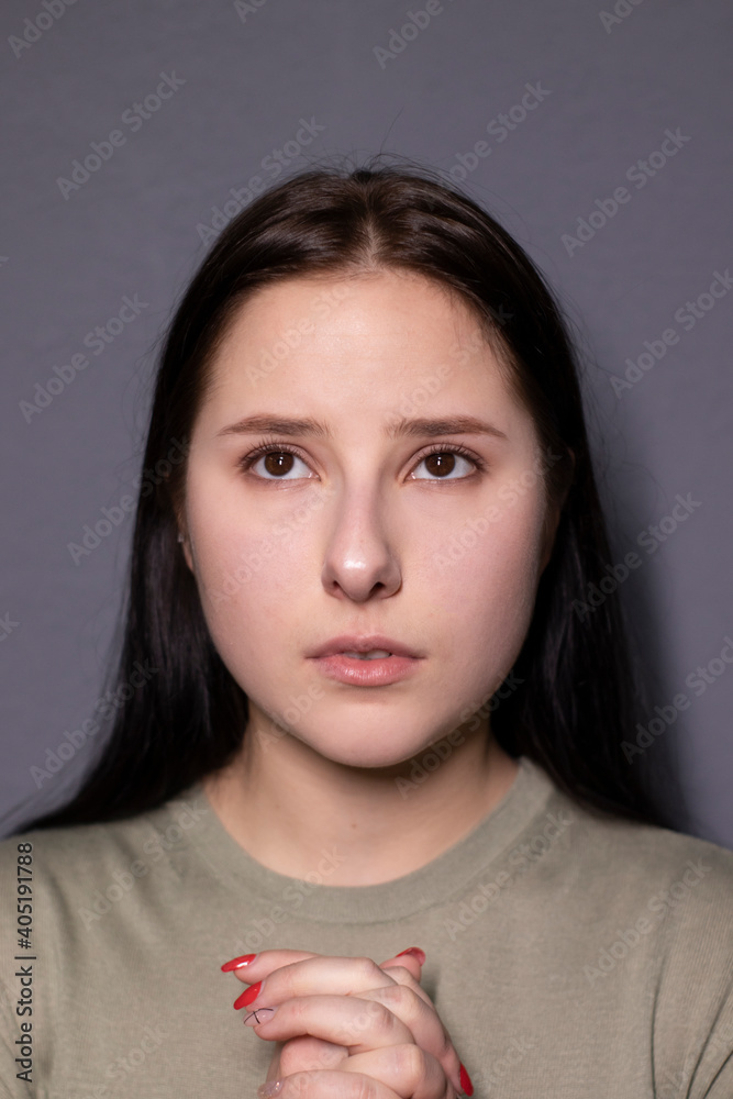 portrait of charming sad brunette woman in marsh color t-shirt on grey wall background. actress acting, emotion
