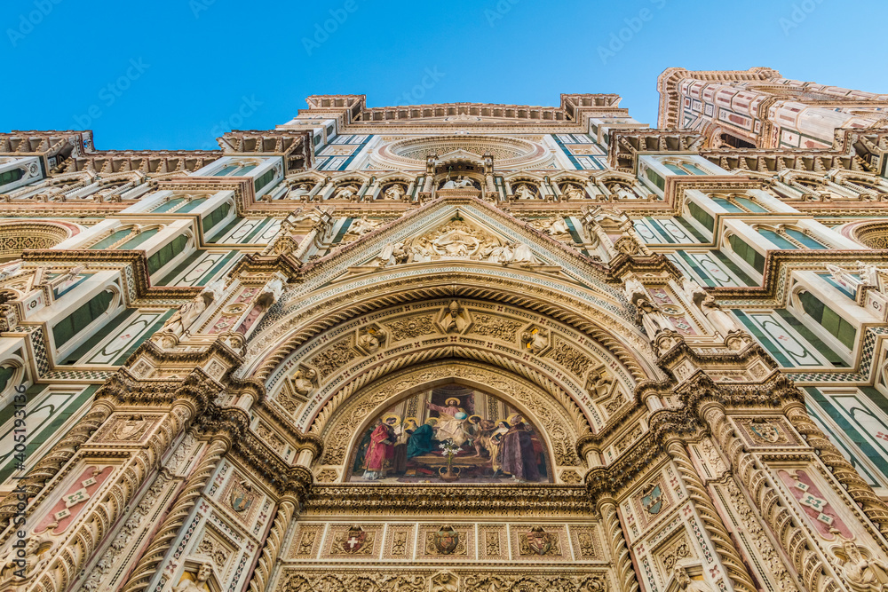 Impressive low-angle view of Florence Cathedral's main facade; from the lunette of the central portal with a colourful mosaic of Christ enthroned, up to the pediment, the rose window and the tympanum.
