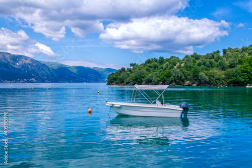 Sea lagoon with calm clear blue water, small white cruise boat, clouds on the sky and mountains on the horizon – summer landscape