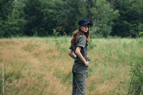 Woman in the woods in a gray jumpsuit blue cap back view 
