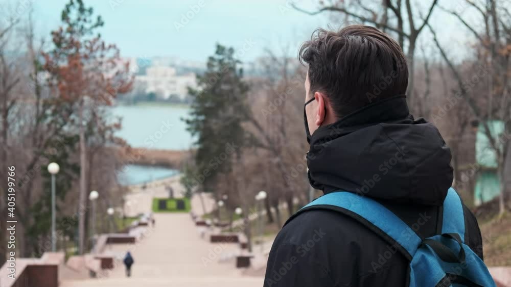 A man in black medical mask and a winter jacket with blue backpack, park on the background in Chisinau, Moldova A man in black medical mask and a winter jacket with blue backpack, park on the background in Chisinau, Moldova