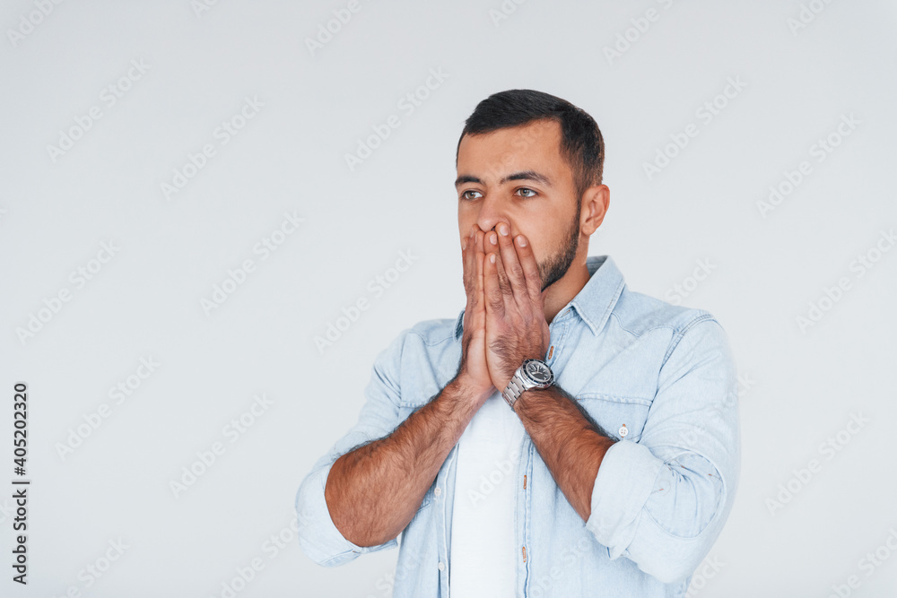 Feels shocked. Young handsome man standing indoors against white background Feels shocked. Young handsome man standing indoors against white background