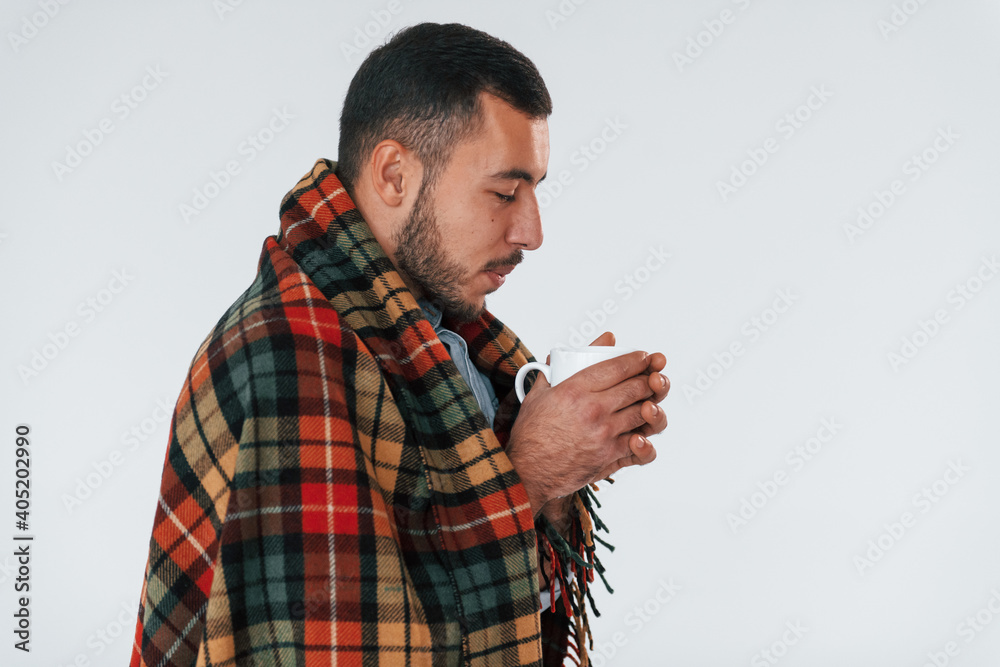 In warm clothes. Feels sick. Young handsome man standing indoors against white background In warm clothes. Feels sick. Young handsome man standing indoors against white background