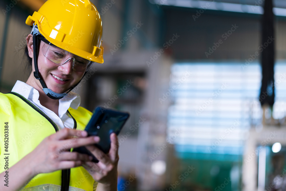Factory Asian woman worker or technician using smartphone chatting Online Messaging with her co-worker engineer in workplace during concern about covid-19 pandemic affect industrial business ,exports