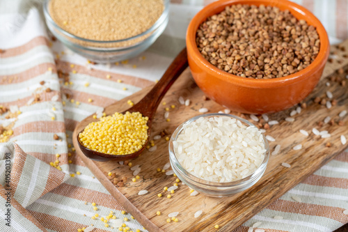 Rice, buckwheat, amaranth and millet in bowls on a brown wooden table. Gluten-free cereals