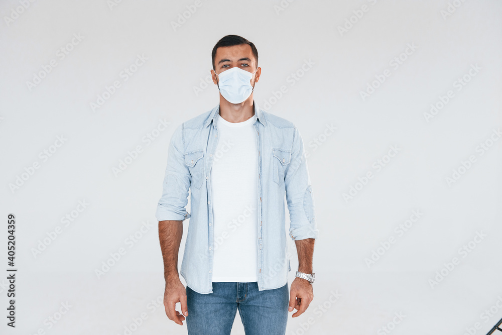 In protective mask. Young handsome man standing indoors against white background In protective mask. Young handsome man standing indoors against white background
