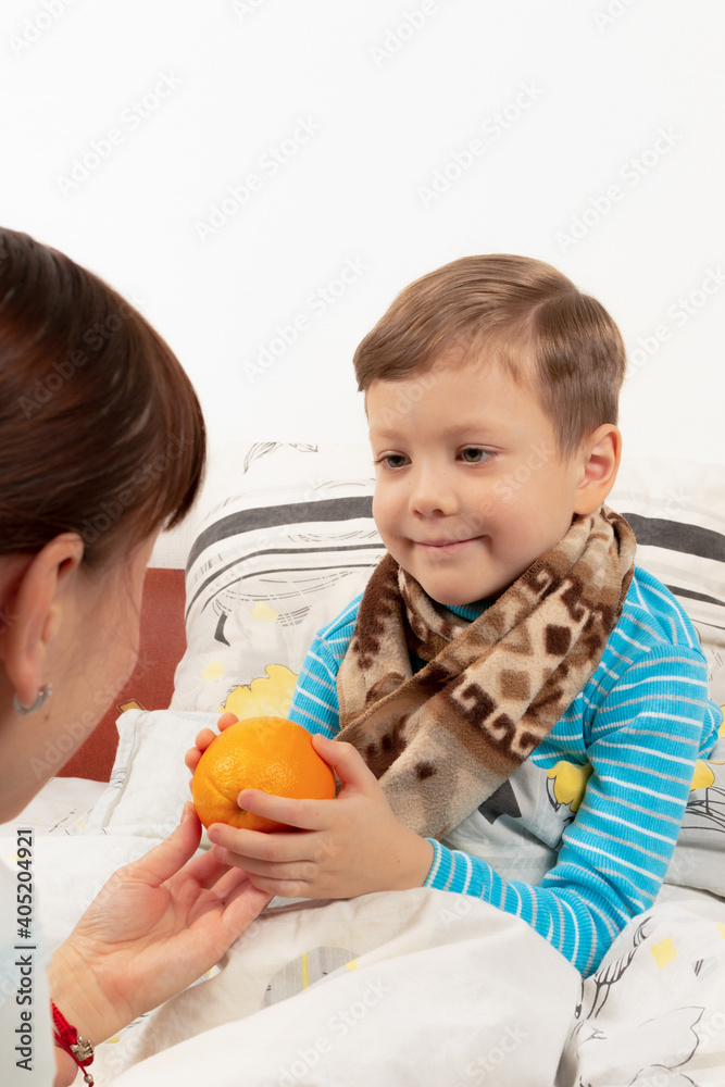 mom carefully gives a sick child a boy wrapped in a warm scarf with a fresh orange mom carefully gives a sick child a boy wrapped in a warm scarf with a fresh orange