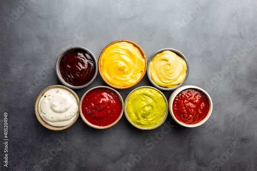 Set of different bowls of various dip sauces, on dark background, top view photo