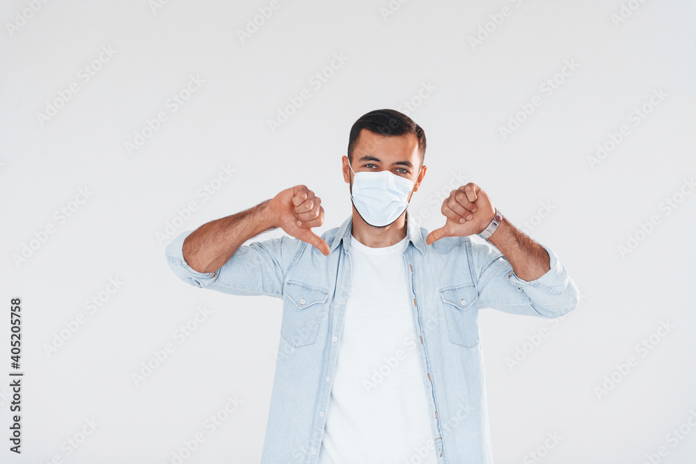 In protective mask. Young handsome man standing indoors against white background