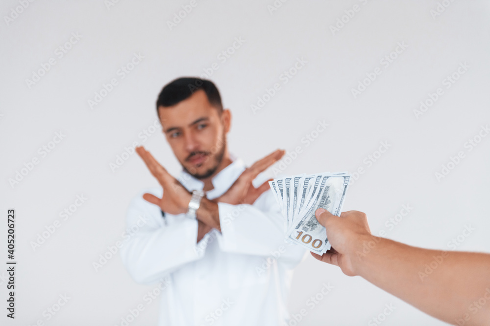 Medic won't take bribe. Young handsome man standing indoors against white background Medic won't take bribe. Young handsome man standing indoors against white background