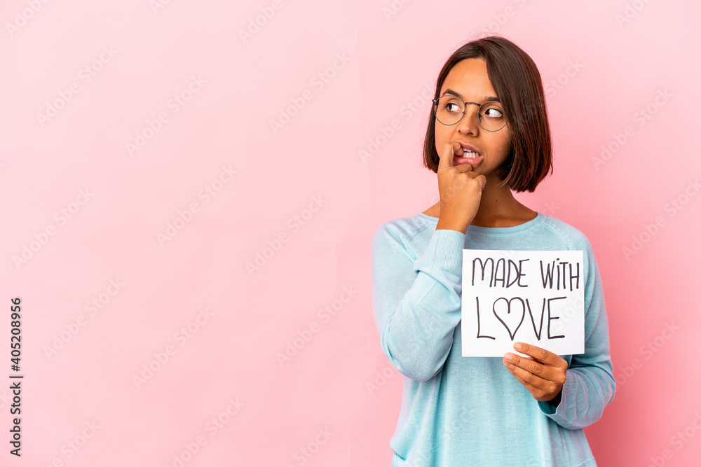 Young hispanic mixed race woman holding a made with love paper poster relaxed thinking about something looking at a copy space. Young hispanic mixed race woman holding a made with love paper poster relaxed thinking about something looking at a copy space.