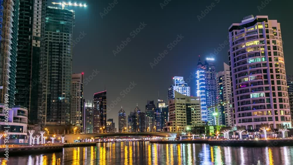 Dubai Marina promenade with yachts and modern towers reflected in water from waterfront in Dubai night timelapse, United Arab Emirates. Bridge and skyscrapers Dubai Marina promenade with yachts and modern towers reflected in water from waterfront in Dubai night timelapse, United Arab Emirates. Bridge and skyscrapers