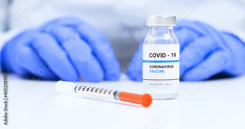 Female doctor hands in blue medical gloves with transparent liquid coronavirus vaccine bottle and syringe for injection in the laboratory. Research and development of new cure for diseases