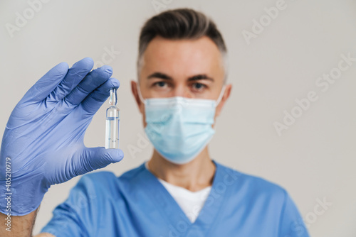 Medical doctor in face mask and gloves showing vial with drug at camera