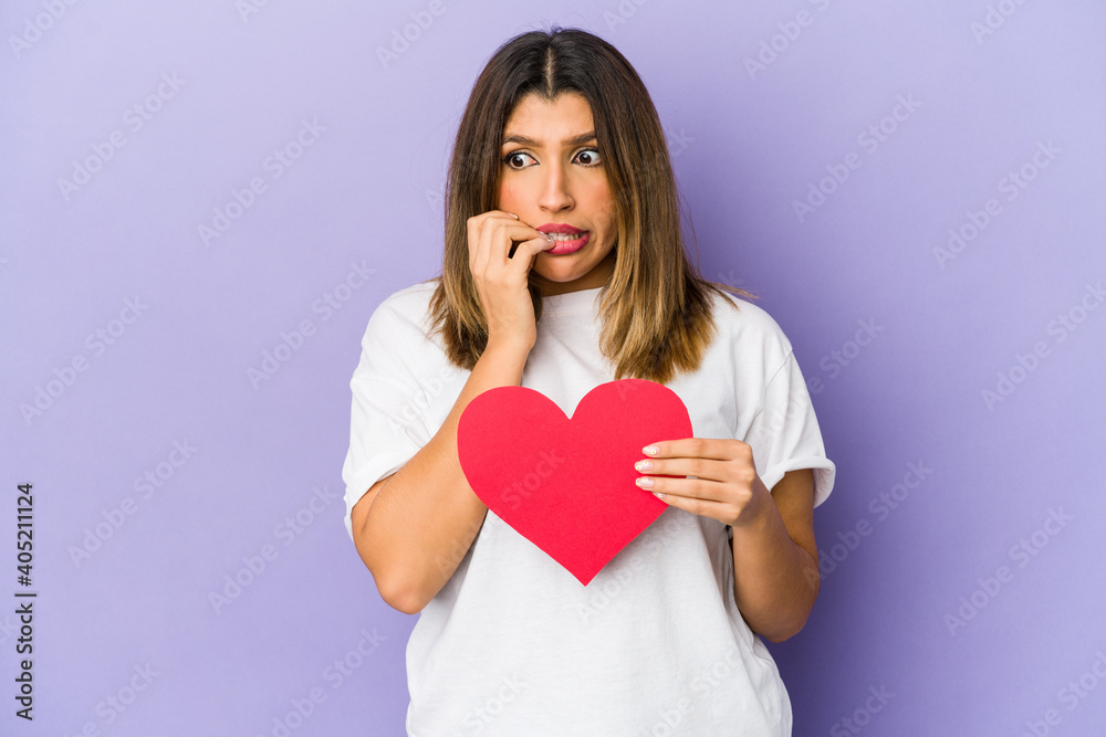 Young indian woman holding a valentines day heart isolated biting fingernails, nervous and very anxious. Young indian woman holding a valentines day heart isolated biting fingernails, nervous and very anxious.