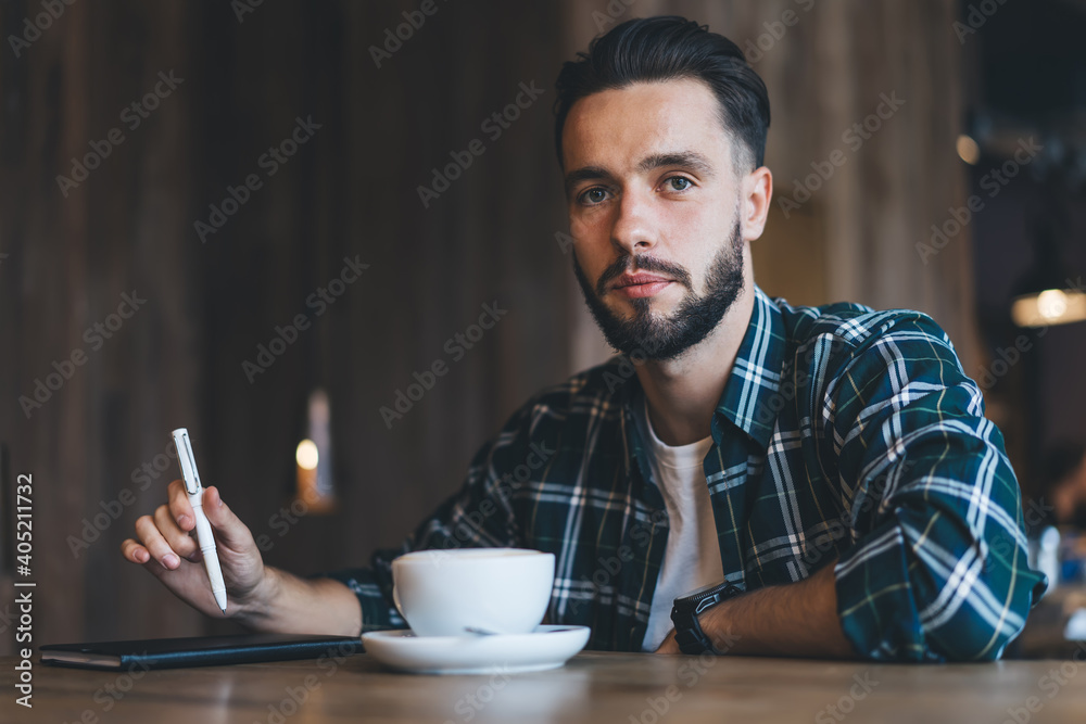 Portrait of Caucasian male journalist with textbook for planning sitting in local cafeteria with tea cup and looking at camera,handsome hipster guy with cappuccino and education notepad in coffee shop Portrait of Caucasian male journalist with textbook for planning sitting in local cafeteria with tea cup and looking at camera,handsome hipster guy with cappuccino and education notepad in coffee shop