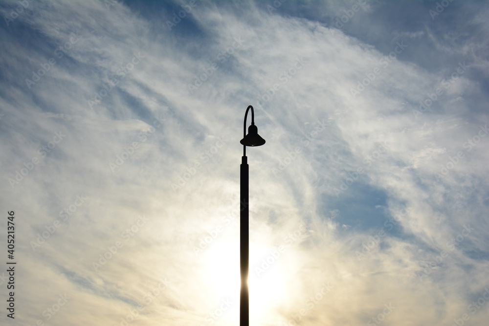 Silhouette of a Street Lamp against the sun with clouds and blue sky