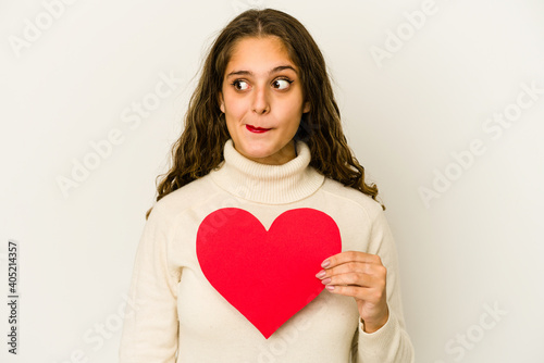 Young caucasian woman holding a heart valentines day shape isolated confused, feels doubtful and unsure.