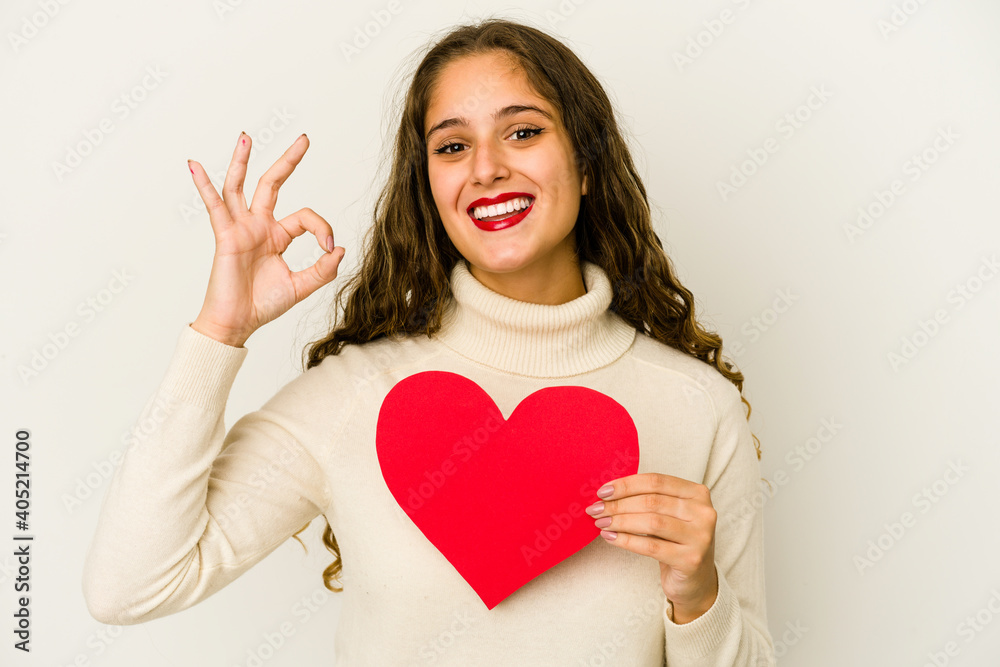 Young caucasian woman holding a heart valentines day shape isolated cheerful and confident showing ok gesture. Young caucasian woman holding a heart valentines day shape isolated cheerful and confident showing ok gesture.