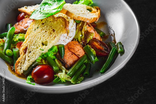 Green Bean Salad with Boiled Eggs, Salmon, Tomatoes and Arugula in a bowl on Dark grey black slate background
