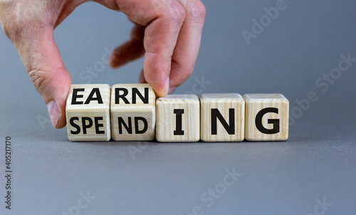 Earning or spending symbol. Businessman hand turns cubes and changes the word 'spending' to 'earning'. Beautiful grey background, copy space. Business and earning or spending concept.