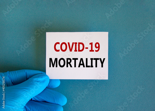 Covid-19 mortality symbol. Hand in blue glove with white card. Concept words 'Covid-19 mortality'. Medical and COVID-19 pandemic mortality concept. Copy space.