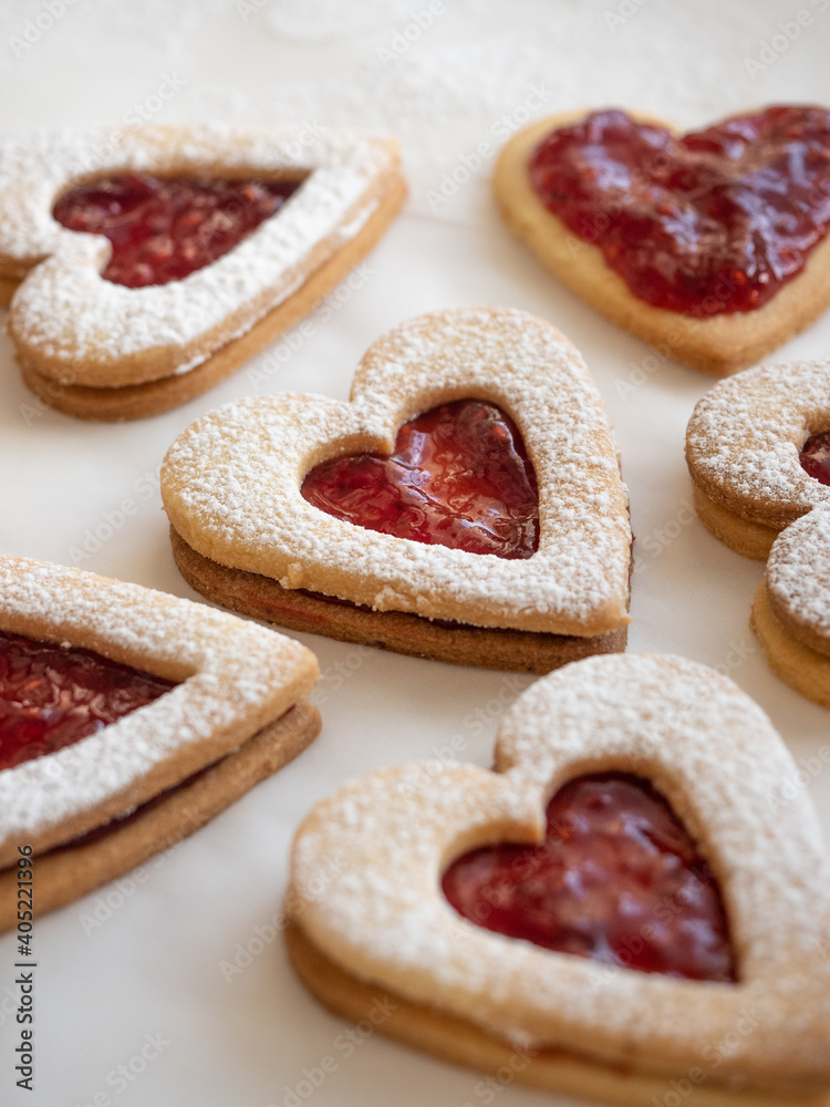 Homemade heart shaped cookies with raspberry jam sprinkled with icing sugar on white background in morning light