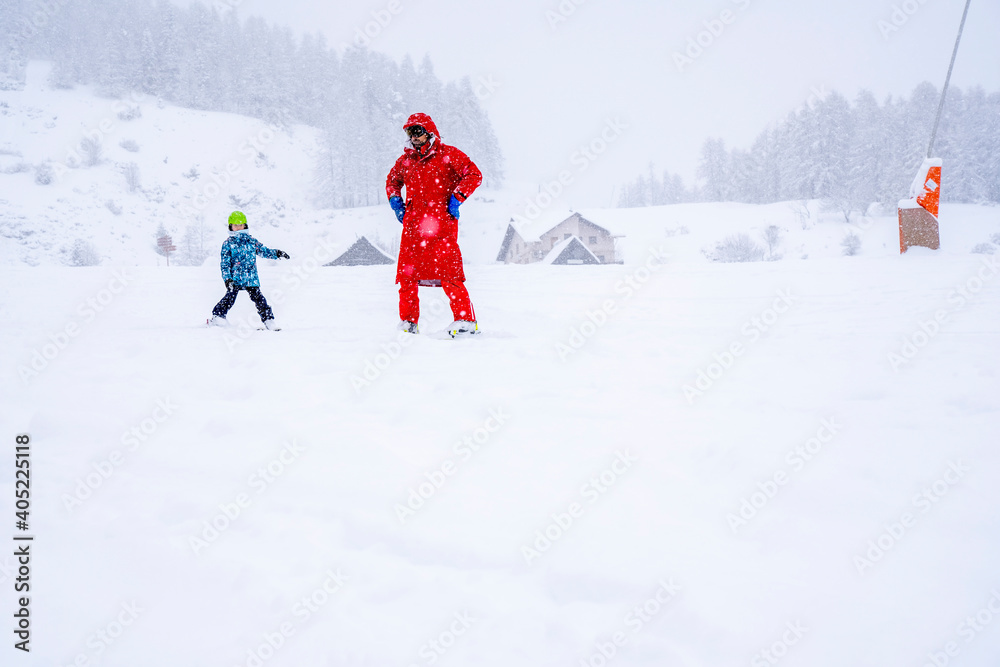 AURON, FRANCE- 01.01.2021: Professional ski instructor is teaching a child to ski on a mountain slope. Snowfall day. Family and children active vacation concept. Blurred focus background. 