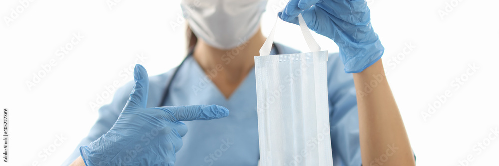 Fototapeta premium Female doctor holding face protective mask in rubber gloves and pointing finger close-up. Covid-19 prevention concept
