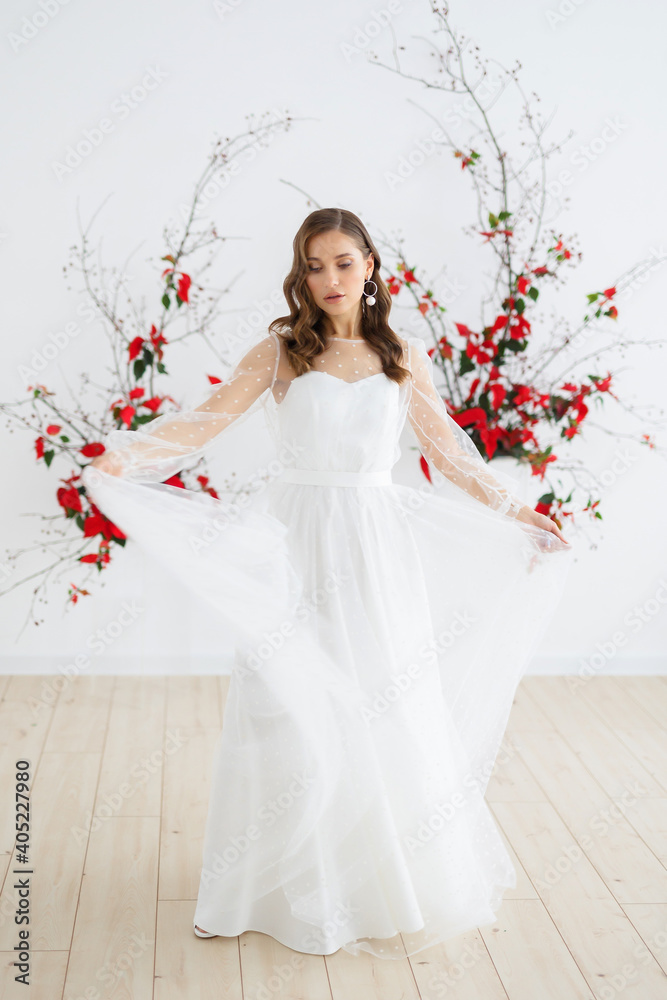 Bride in a white wedding dress poses against the background of an unusual composition of natural poinsettia flowers for a chamber wedding ceremony. Spins around in a dress and holds it in her hands. Bride in a white wedding dress poses against the background of an unusual composition of natural poinsettia flowers for a chamber wedding ceremony. Spins around in a dress and holds it in her hands.