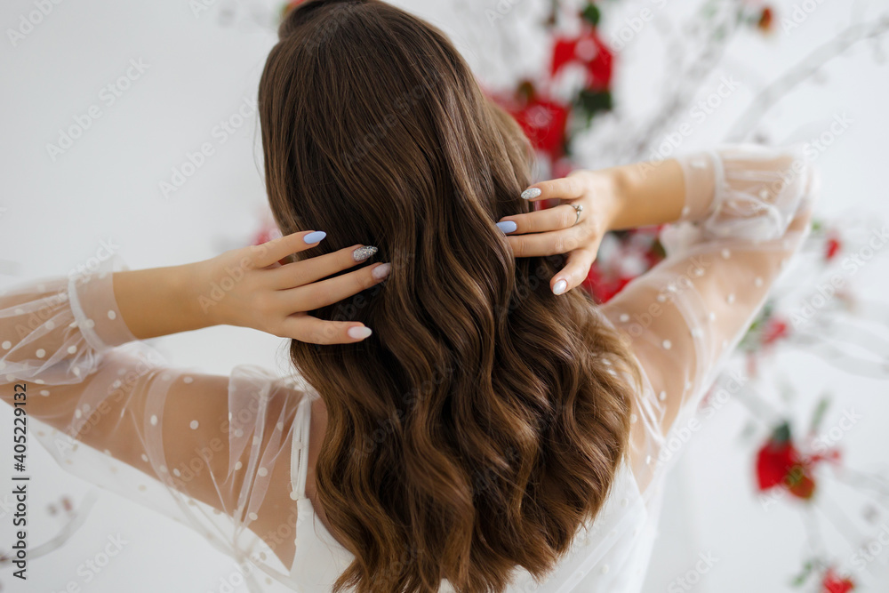 Girl model holds her brunette hair. Wedding and evening styling and hairstyling