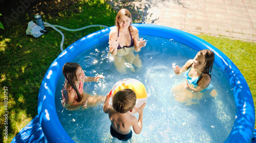 Happy laughing children with mother having fun and playing with inflatable ball in swimming yard. Family summer vacation and holidays