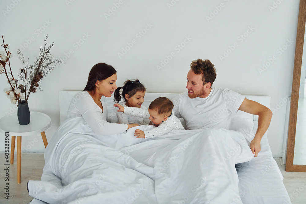 Woman and man lying down on bed with their children. Interior and design of beautiful modern bedroom at daytime Woman and man lying down on bed with their children. Interior and design of beautiful modern bedroom at daytime