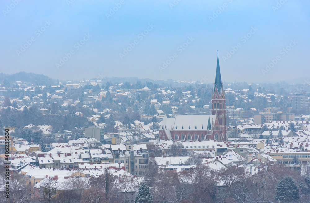 Cityscape of Graz with Church of the Sacred Heart of Jesus and historic buildings rooftops with snow, in Graz, Styria region, Austria, in winter