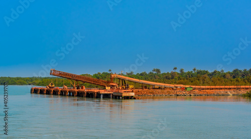 Outdoor industrial jetty at river bank with incline large conveyor for transportation bauxite ore from mining shuttle trains to feeder ships. Guinea, West Africa.
