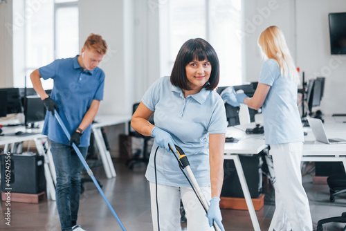 Woman uses vacuum cleaner. Group of workers clean modern office together at daytime
