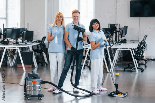 Guy with vacuum cleaner. Group of workers clean modern office together at daytime