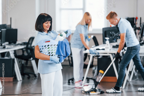 Woman with basket. Group of workers clean modern office together at daytime