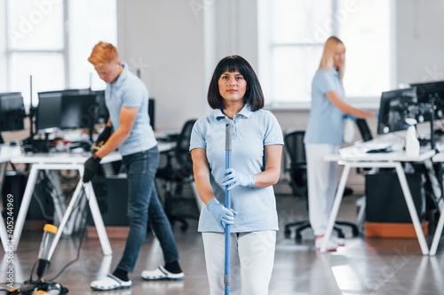 Cleans floor. Group of workers clean modern office together at daytime