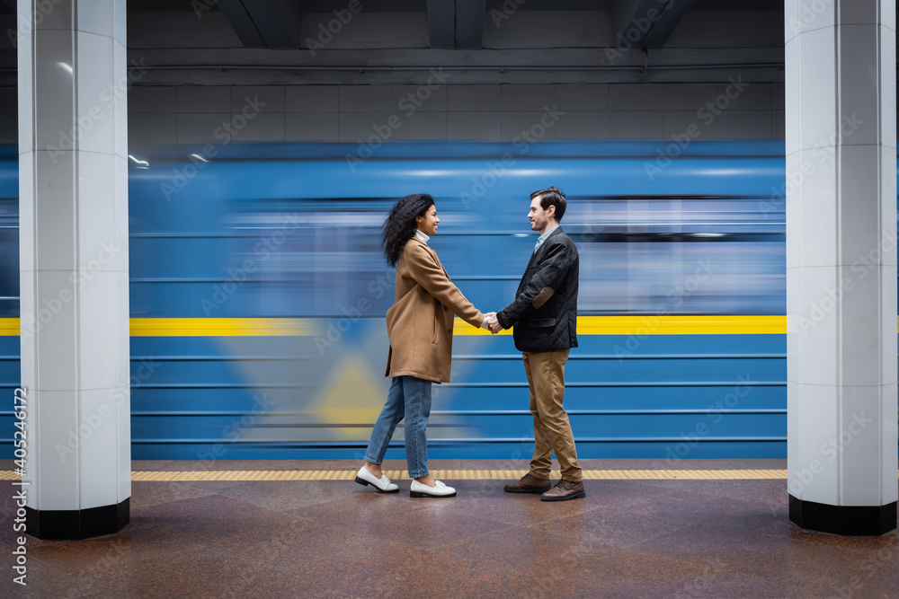 Fototapeta premium long exposure of interactional couple holding hands while standing near wagon in subway