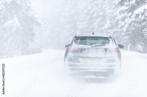 Car covered in snow driving in snowstorm on a cold winter day in the forest